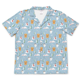 A short-sleeve button-up camp shirt in light blue, featuring an all-over print of golden retriever dogs, white dogs, snowmen, Christmas trees, and snowflakes.