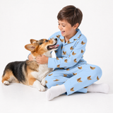 Child in sky blue pajamas with dog pattern sitting on a white surface with a dog.