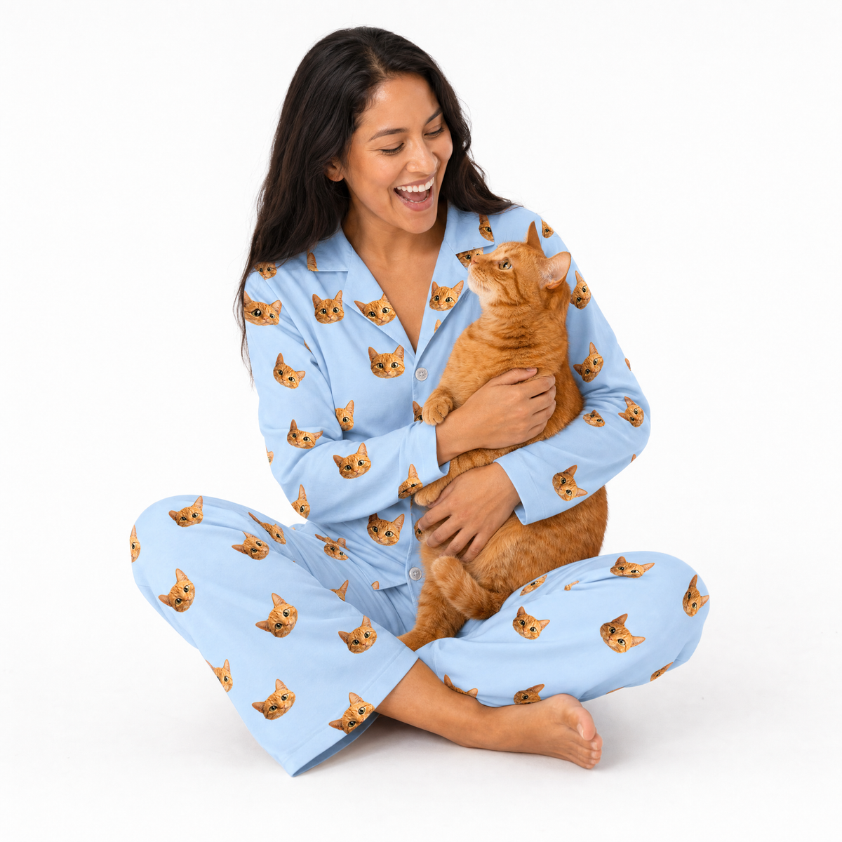 Woman wearing a sky blue pajama set with cat pattern, holding an orange cat on a white background