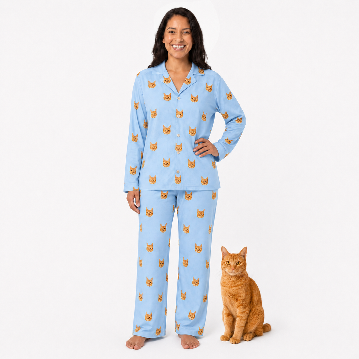Woman wearing sky blue pajamas with cat pattern standing next to an orange cat on a white background