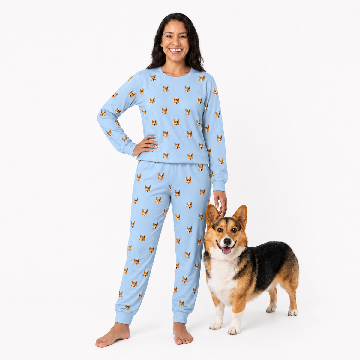 Woman wearing a light blue jogger pajama set with dog pattern, standing next to a corgi on a white background