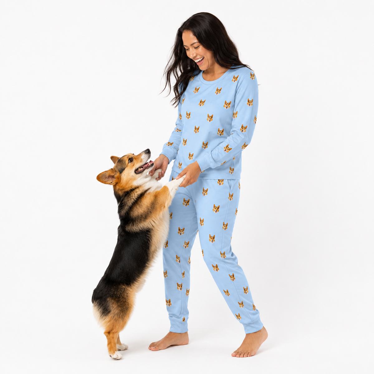 Woman wearing a Sky Blue dog-print pajama set holding paws with a corgi standing on its back legs.