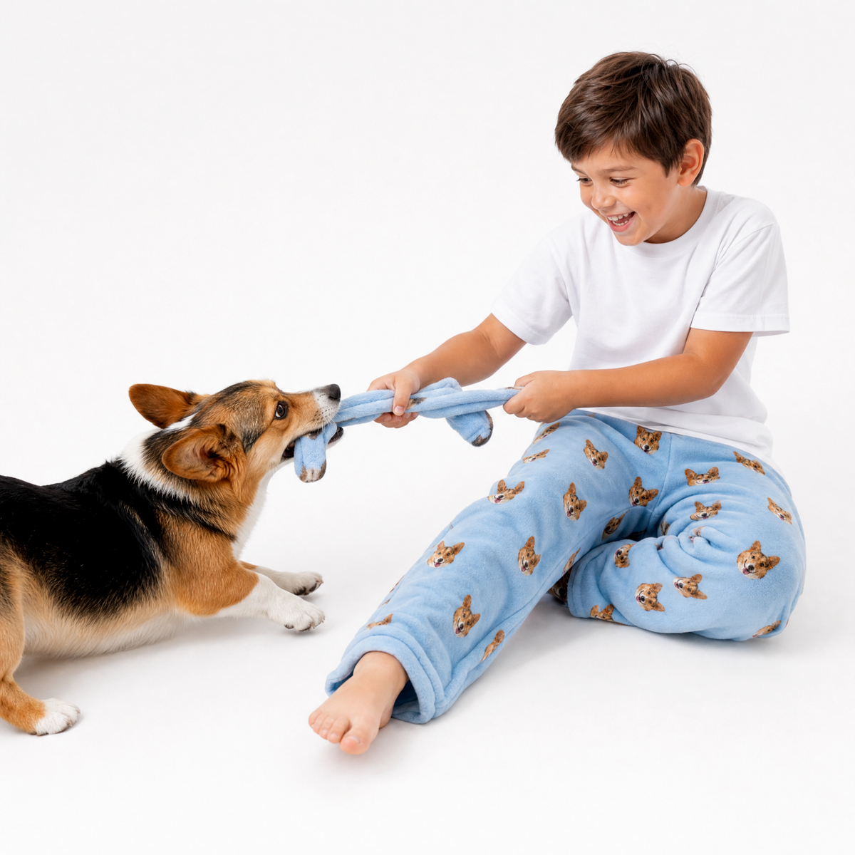 Sky blue theme – child in dog-print pajamas playing tug-of-war with corgi.