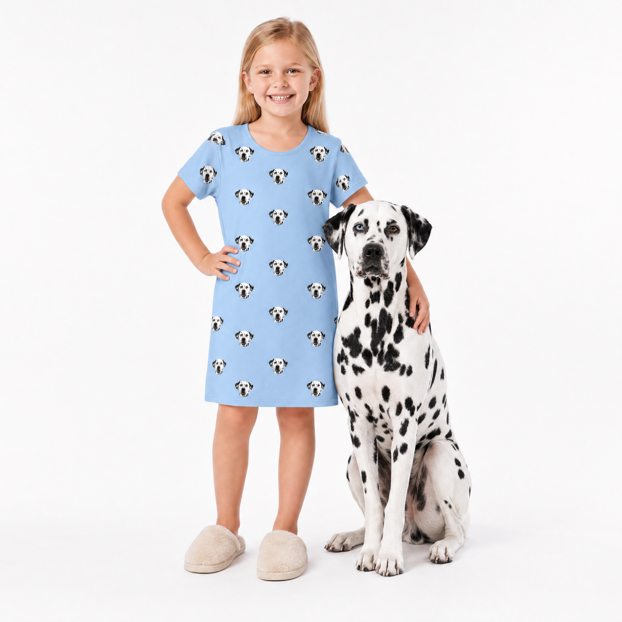 Girl in a sky blue nightgown with dog pattern standing next to a Dalmatian dog on a white background