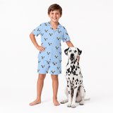 Child wearing a sky blue pajama set with dog pattern standing next to a Dalmatian dog on a white background