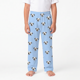 A child wearing sky blue pants with an all-over print of black-and-white dog faces, paired with a plain white top, standing against a light gray studio background.