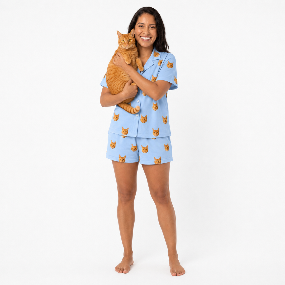 Woman wearing a sky blue pajama set with cat patterns, holding an orange cat on a white background.