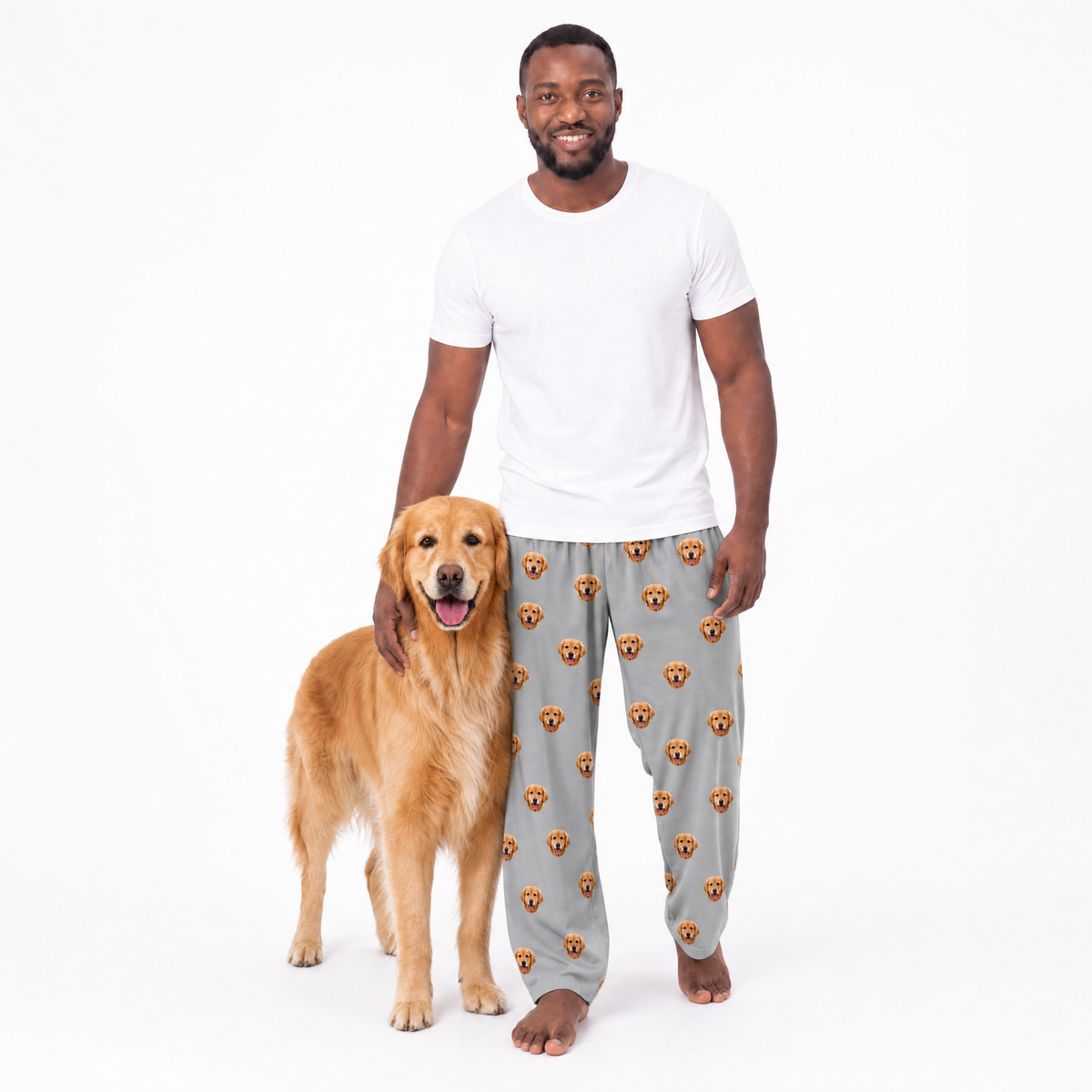 Man wearing gray pajama pants with dog pattern standing next to a golden retriever on a white background