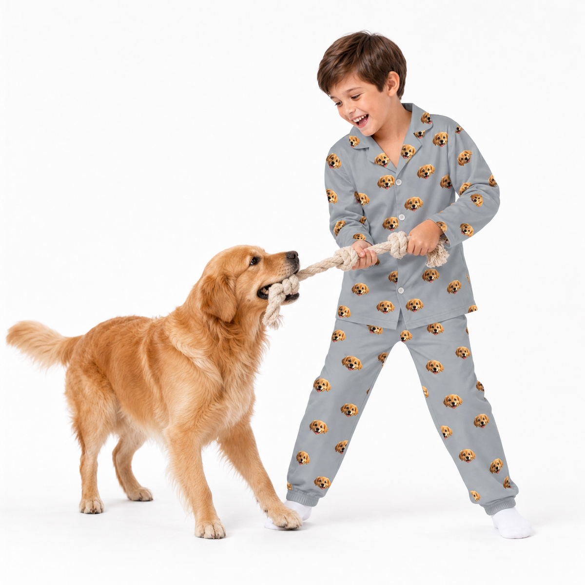 Child in gray pajamas playing tug of war with a dog on a white background
