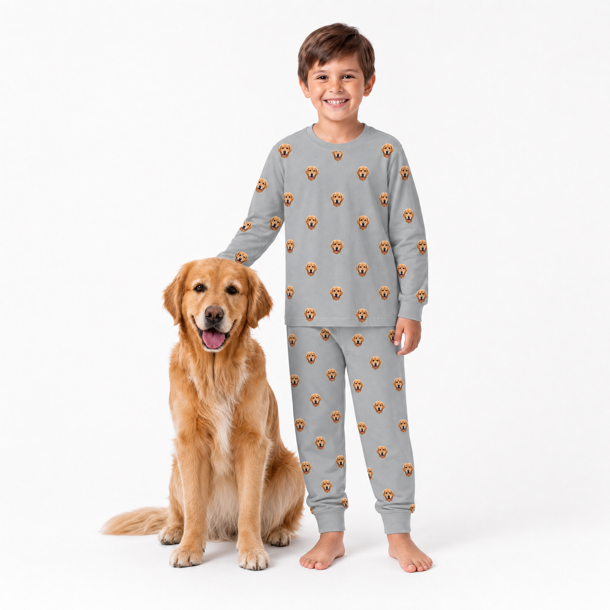 Child wearing a gray jogger pajama set with dog faces, standing next to a golden retriever on a white background