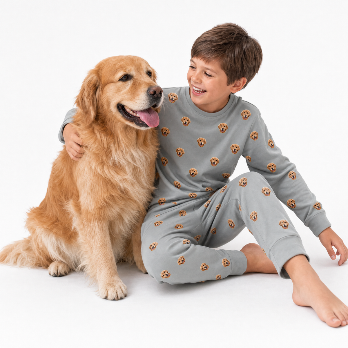 Child in a gray jogger pajama set with dog patterns sitting next to a golden retriever on a white background