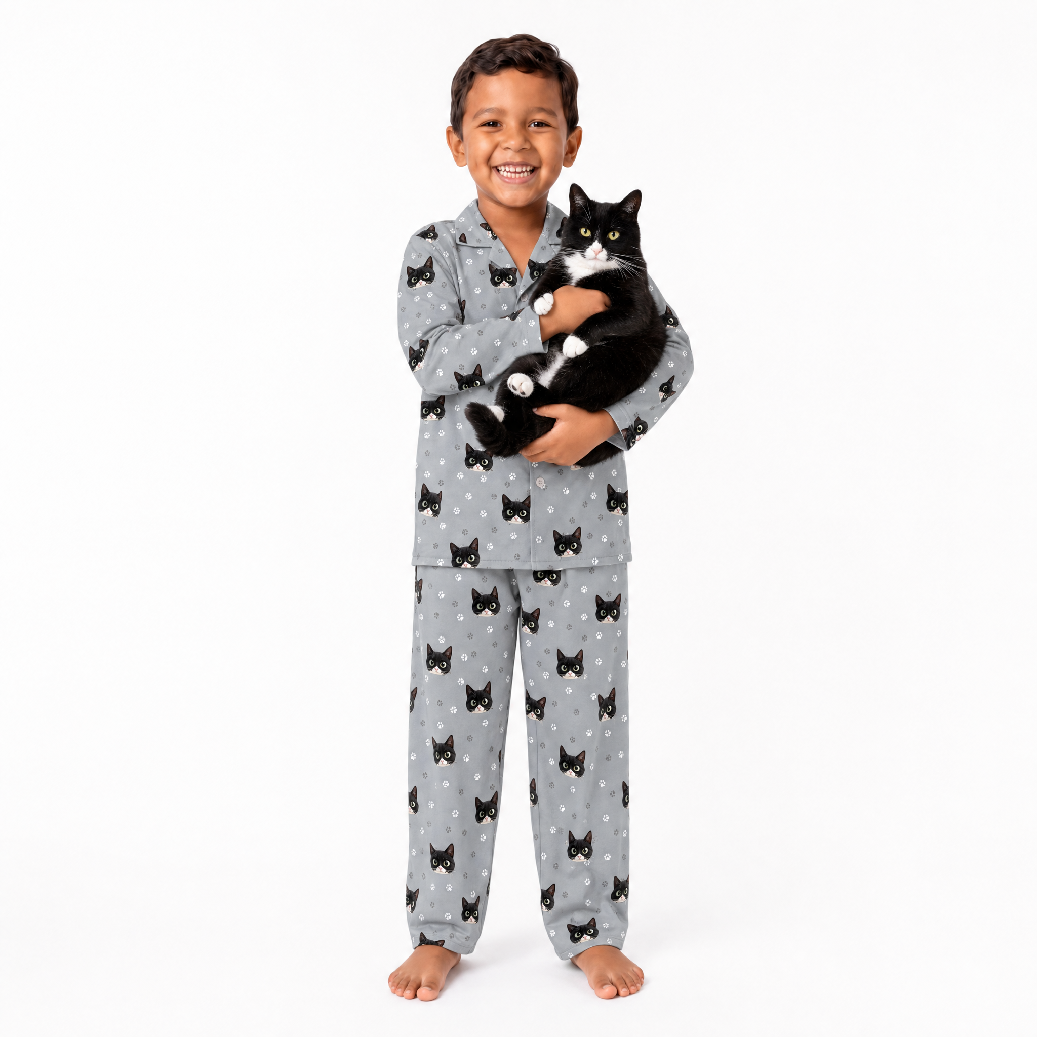 Child wearing gray pajamas with black cat patterns, holding a black and white cat on a white background