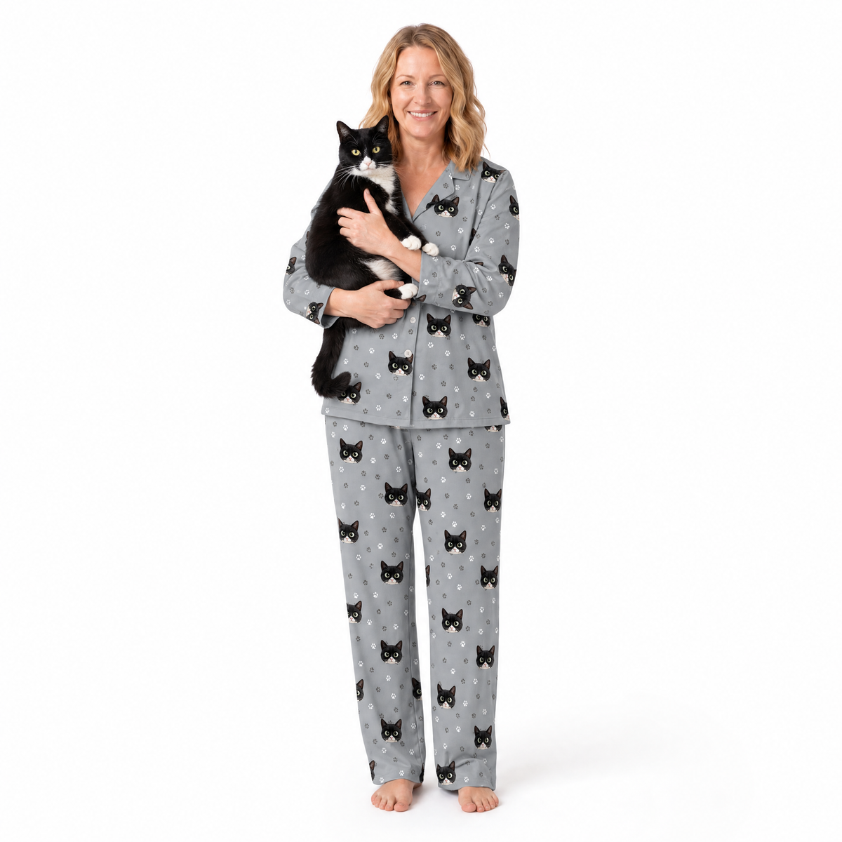 Woman wearing a gray pajama set with black cat patterns, holding a black and white cat on a white background.