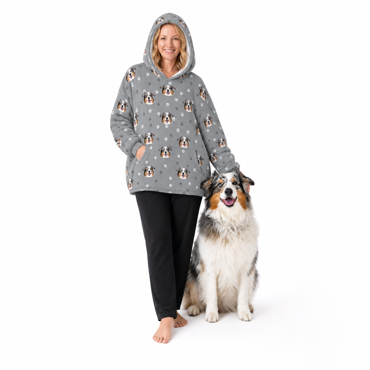 Person wearing a gray blanket hoodie with dog patterns standing next to a dog on a white background