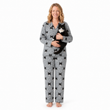 Woman wearing gray pajamas with black bow pattern, holding a black and white cat on a white background