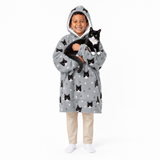 Child wearing a gray blanket hoodie with black cat patterns, holding a black and white cat on a white background.
