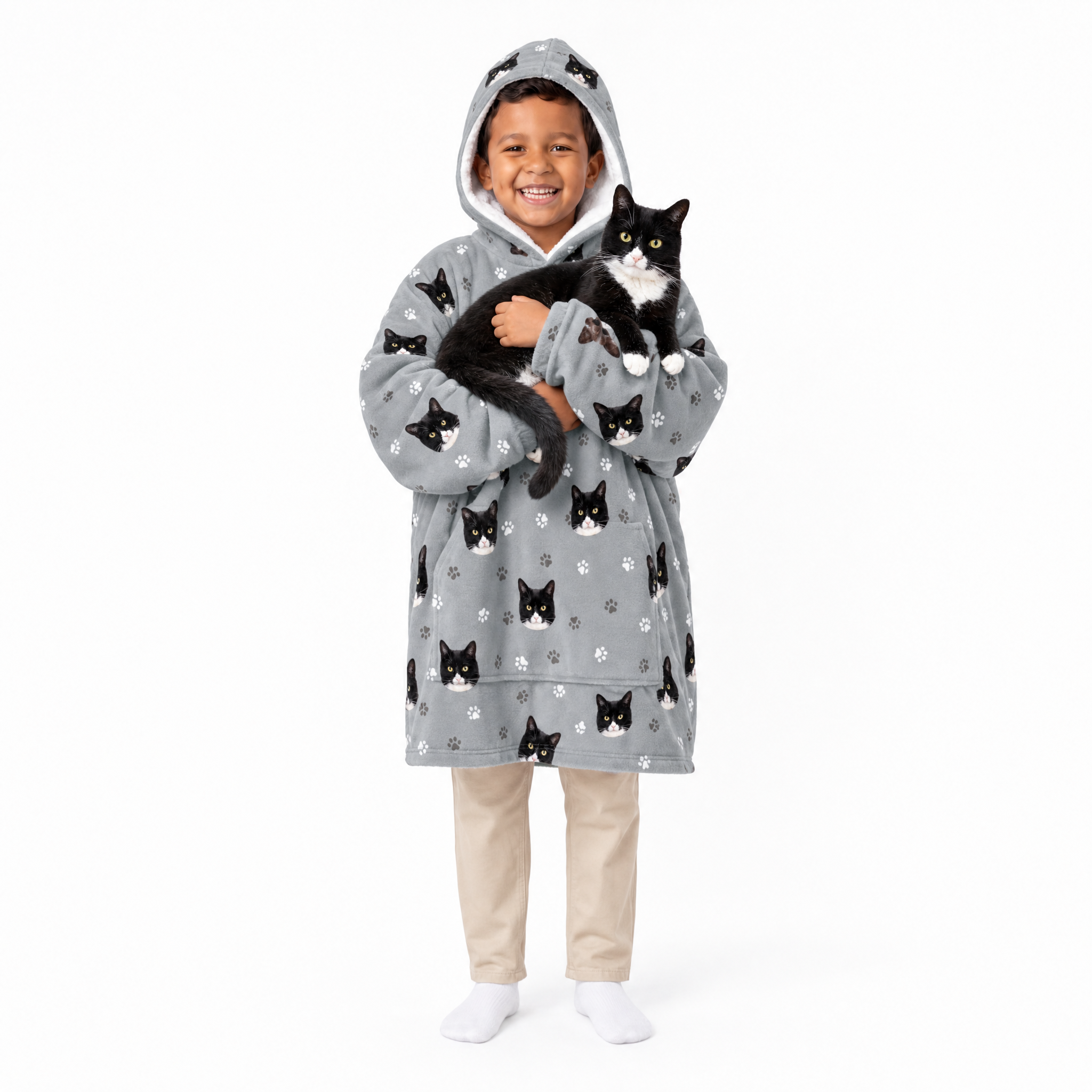 Child wearing a gray blanket hoodie with black cat patterns, holding a black and white cat on a white background.