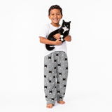 Child wearing a white shirt and gray  pajama pants holding a black and white cat on a white background