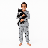 Child wearing a gray jogger pajama set with cat patterns, holding a black and white cat on a white background.