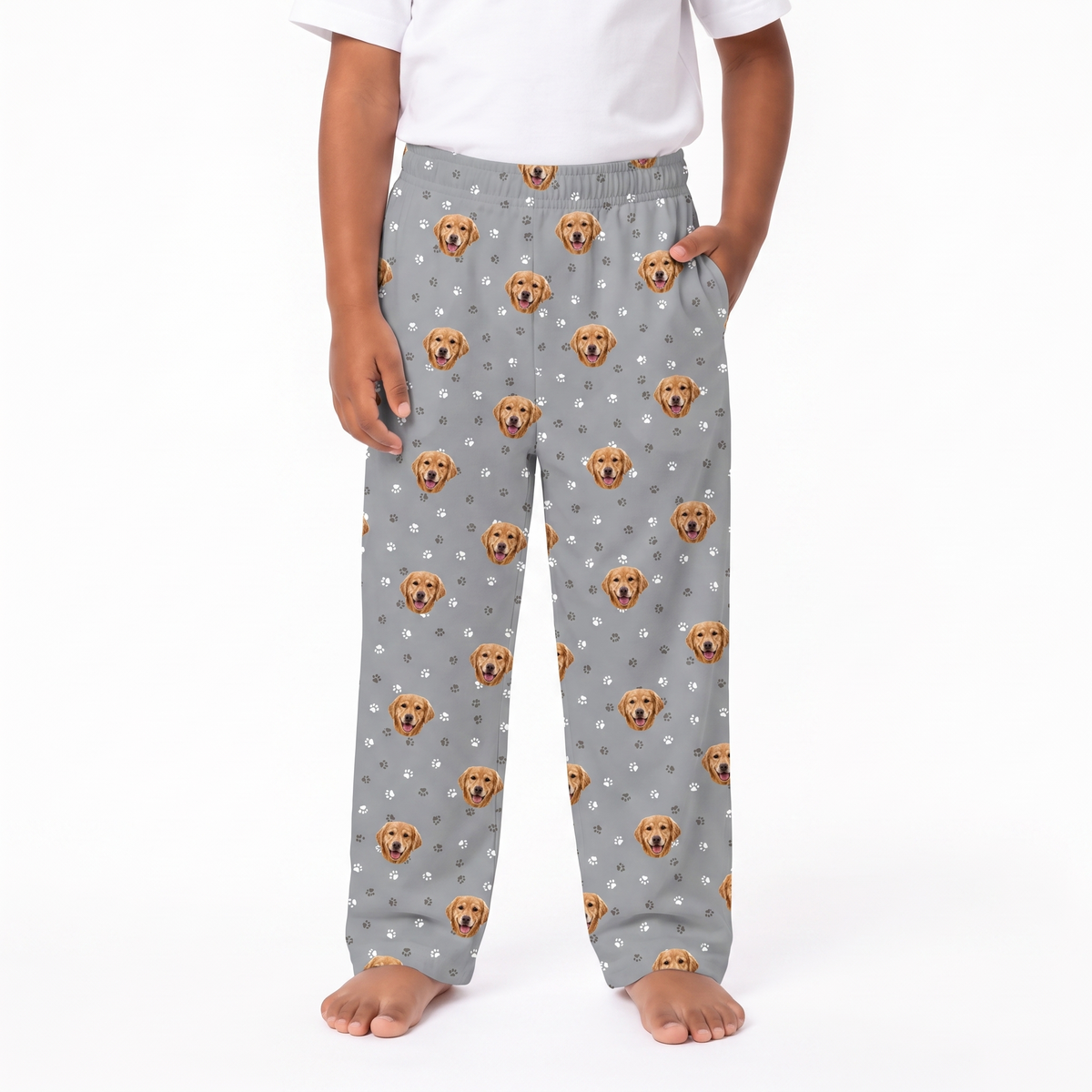 A child wearing slate gray lounge pants with an all-over print of Golden Retriever dog faces and small white paw prints, paired with a plain white t-shirt, shown against a white studio background.
