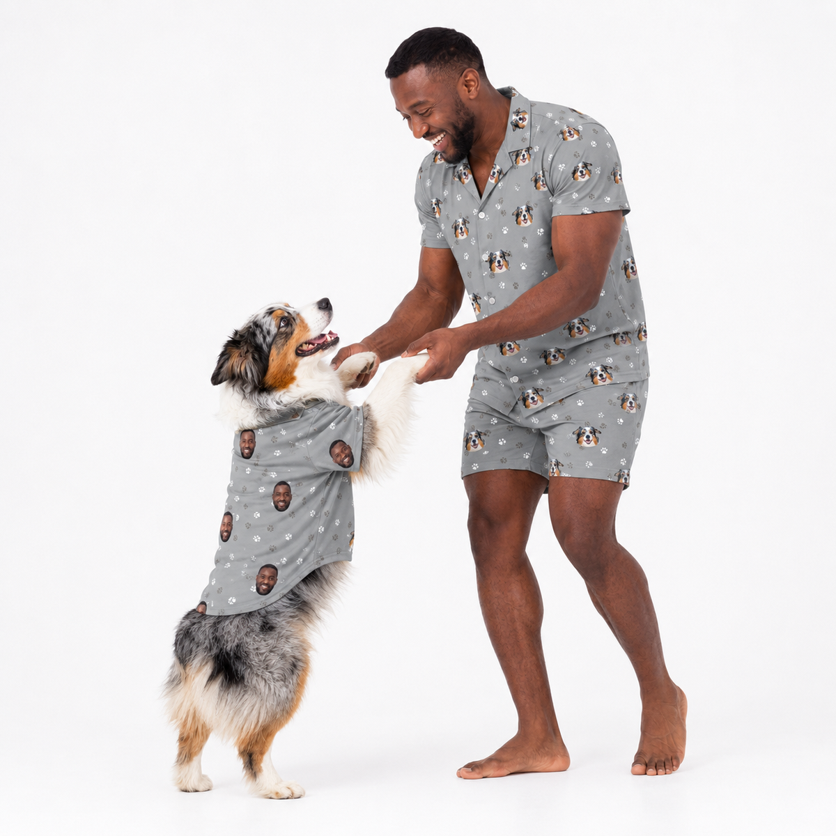 Man and dog wearing matching gray custom pet pajamas with a repeating dog face and paw print pattern.