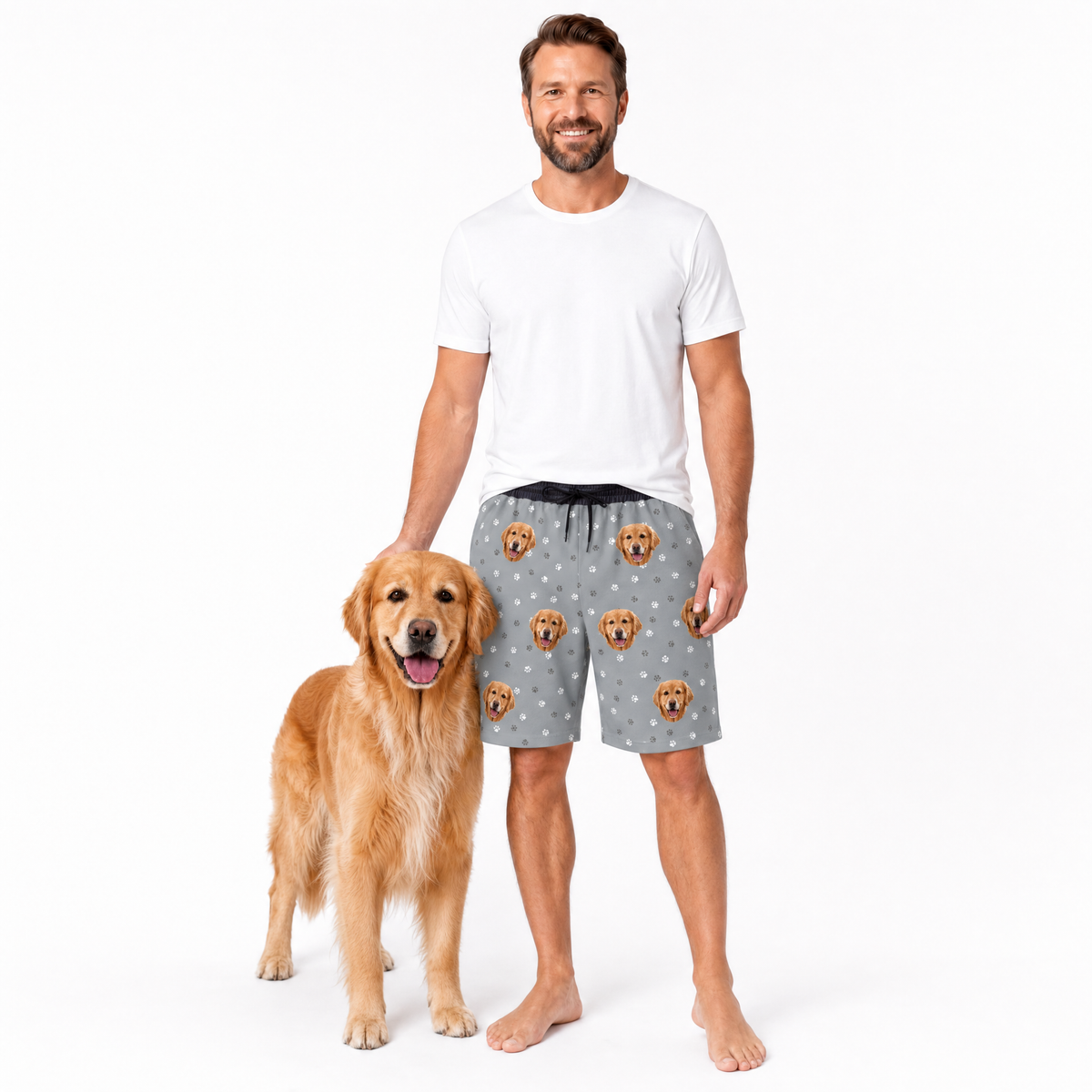 Man wearing gray shorts with dog pattern standing next to a golden retriever on a white background