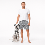 Man wearing a white t-shirt and gray shorts with dog pattern standing next to a Dalmatian dog on a white background