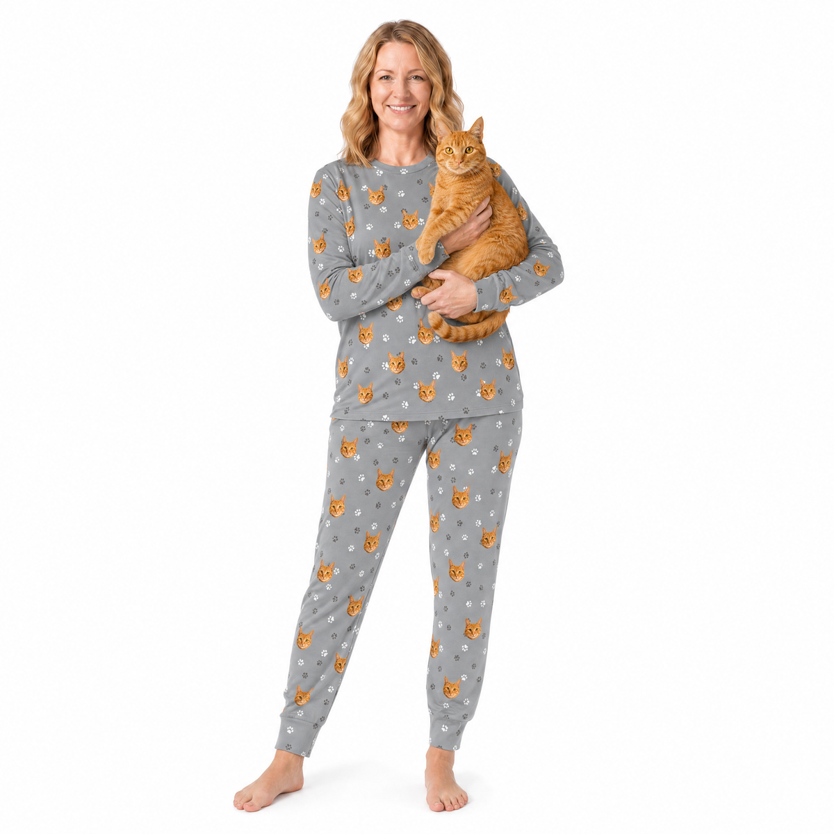 Woman wearing a gray jogger pajama set with orange cat pattern, holding an orange cat on a white background