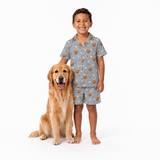Child wearing a gray pajama set with dog pattern standing next to a golden retriever on a white background