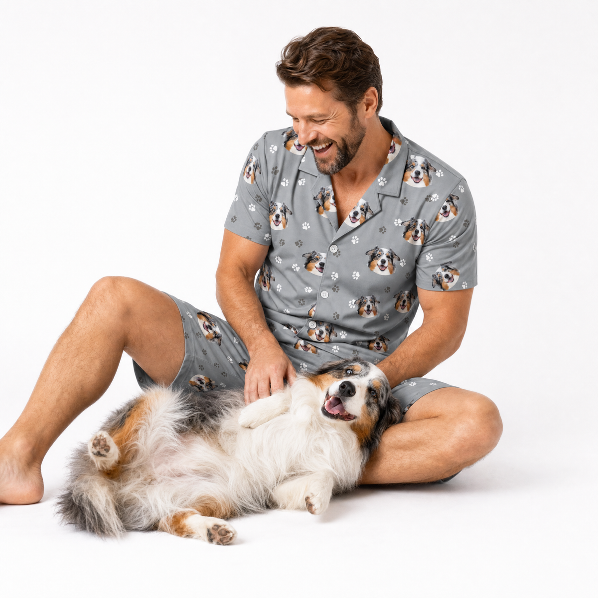 Man in a dog-patterned outfit sitting with a dog on a white background