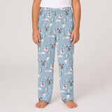 A child wearing light blue pajama pants with a winter dog print, standing barefoot against a plain light gray studio background.