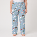 A person wearing light blue pajama pants with an all-over Christmas dog and snowman print, standing barefoot against a plain light gray studio background.