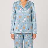 A model wearing a light blue long-sleeve pajama set with a Christmas dog print, featuring a button-up top and matching pants against a light gray studio background.