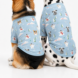 Two dogs sitting side by side wearing matching light blue holiday-themed pet shirts with a snowman and dog print, photographed on a clean white studio background.