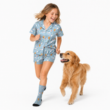 A young girl wearing a light blue pajama set with a dog print and matching socks is running happily next to a golden retriever dog on a white studio background.