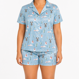 A model wearing a light blue short-sleeve pajama top and matching shorts with a Christmas dog print, shown against a plain white background.