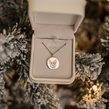 Silver dog-portrait necklace in a box among snowy Christmas branches.