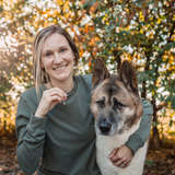 Woman smiling outdoors with an Akita, holding a small necklace charm