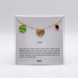 Necklace with heart-shaped pendant, tennis ball charm, and red gemstone on a display card with text.
