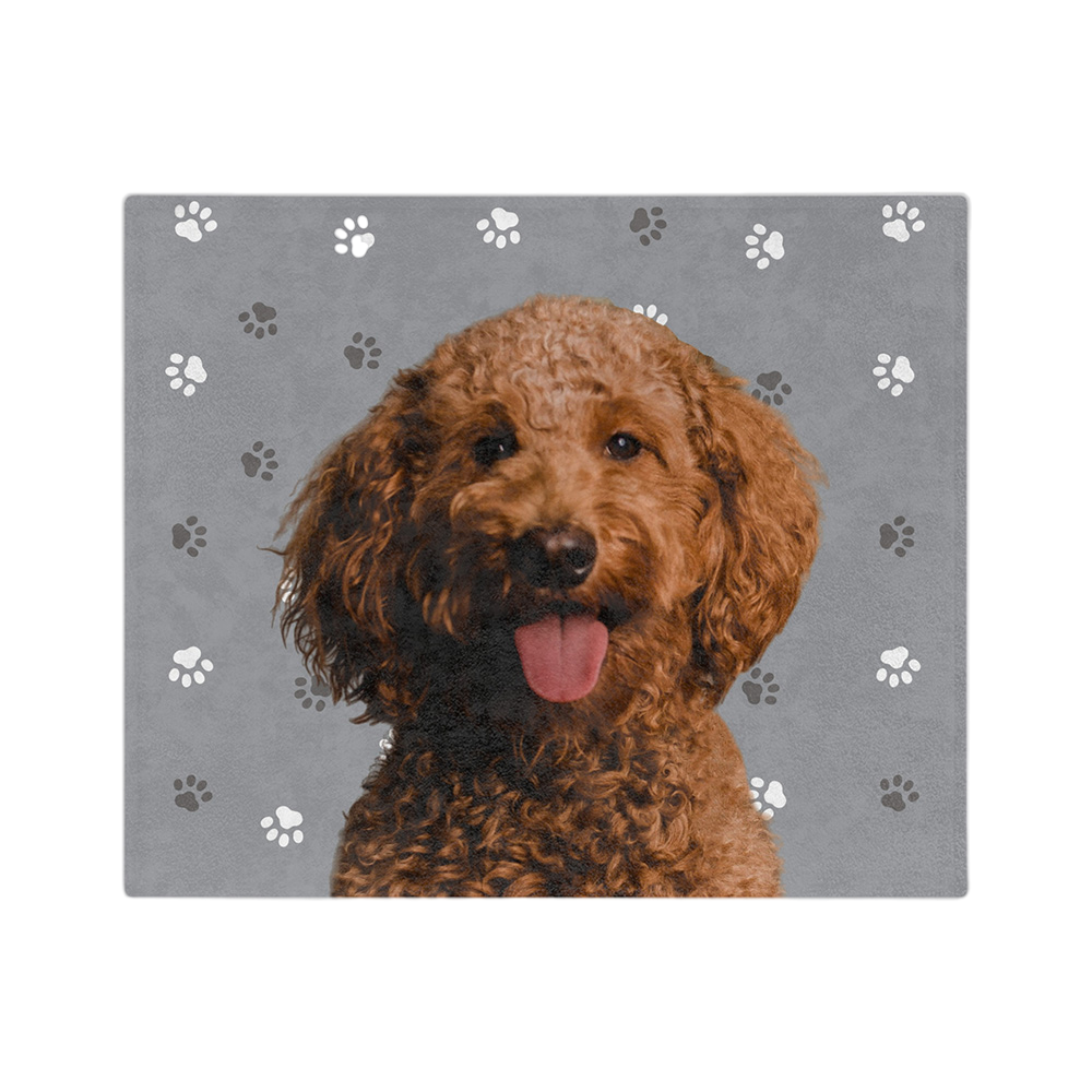 A blanket with a gray background and paw prints, featuring a centered, smiling portrait of a dog.