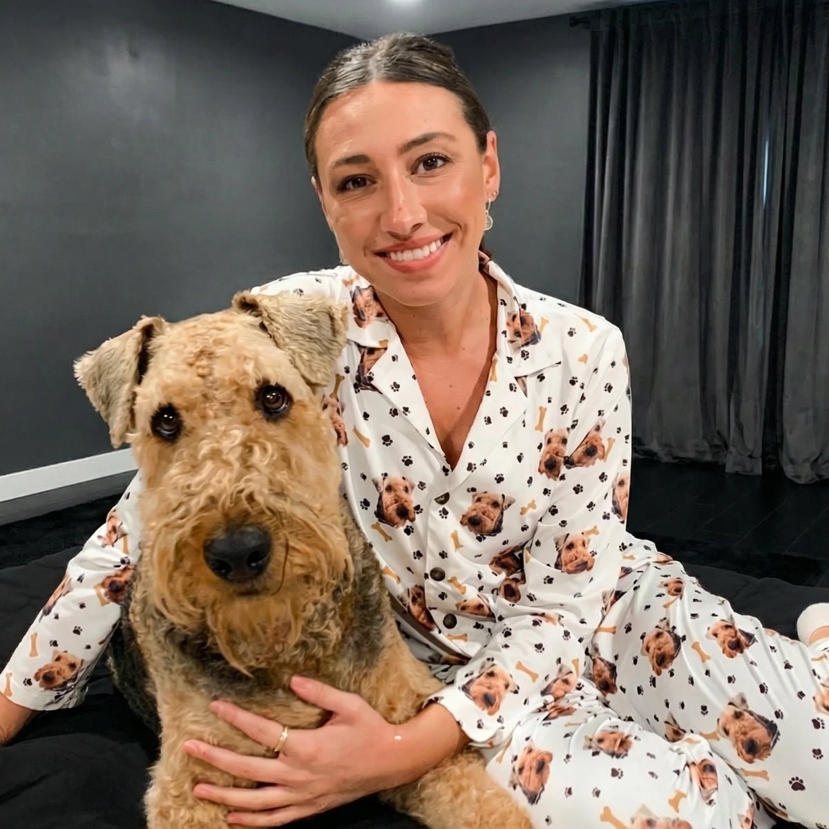 Woman in dog-themed pajamas holding a dog, sitting on a couch.