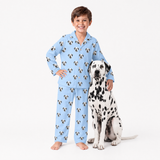 Child wearing sky blue pajamas with dalmatian pattern standing next to a Dalmatian dog on a white background