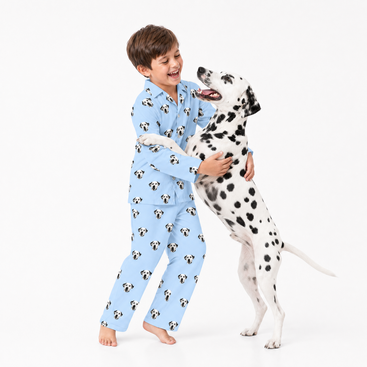 Child in sky blue pajamas with dog pattern hugging a Dalmatian dog on a white background