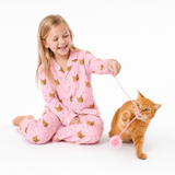 Child in pink pajamas with cat pattern playing with a cat on a white background