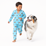 Child wearing a Sky Blue dog-print pajama set running beside a gray and white dog.