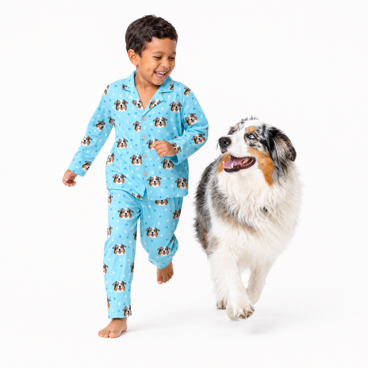 Child wearing light blue pajamas with dog pattern standing next to a dog on a white background