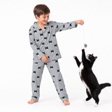 Child wearing a Slate Gray cat-print pajama set playing with a black and white cat using a hanging toy.