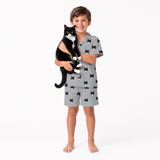 Child wearing a gray pajama set with black cat pattern, holding a black and white cat.