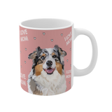 Clos up of a pink ceramic mug with hearts and the phrase "I Love Mom", featuring a smiling, multicolored Australian Shepherd [ILoveMomHandIllustration]