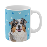 Close up of light blue ceramic mug with paws pattern, featuring a smiling, multicolored Australian Shepherd [LightBluePawsHandIllustaration]